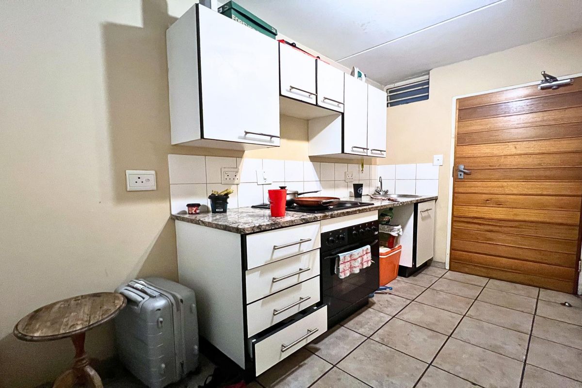 A compact kitchen featuring white cabinetry, a built-in oven, tiled backsplash, and tiled flooring, providing a functional workspace in need of minor cosmetic updates.