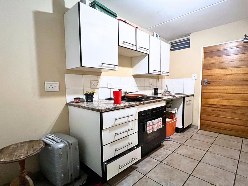A compact kitchen featuring white cabinetry, a built-in oven, tiled backsplash, and tiled flooring, providing a functional workspace in need of minor cosmetic updates.