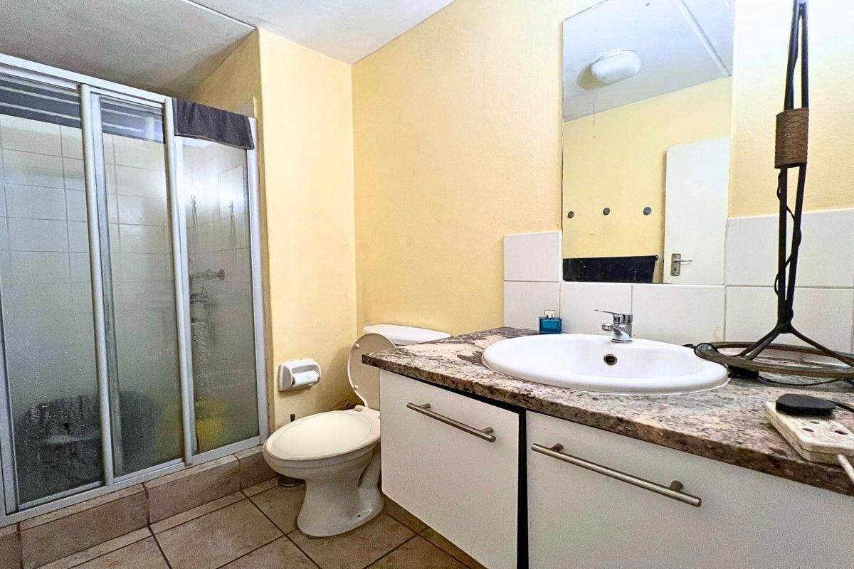 A functional bathroom featuring a shower enclosure, vanity with granite countertop, and wall-mounted mirror, presenting a dated but practical layout.