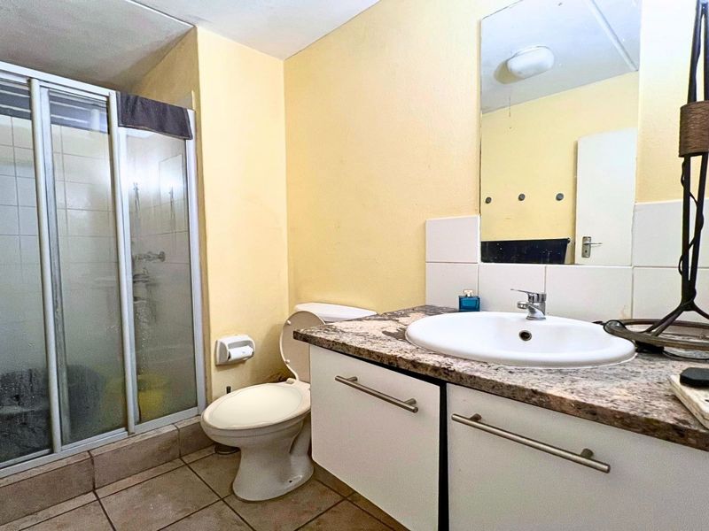 A functional bathroom featuring a shower enclosure, vanity with granite countertop, and wall-mounted mirror, presenting a dated but practical layout.