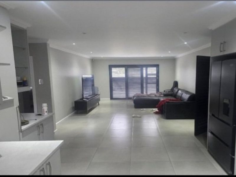 Spacious open-plan living area featuring large format floor tiles, recessed lighting, and modern cabinetry, leading out through sliding doors to an outdoor space.