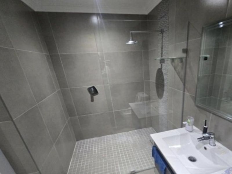 Modern bathroom featuring a spacious walk-in shower with a rain shower head, glass screen, and a sleek vanity basin with a wall-mounted mirror.
