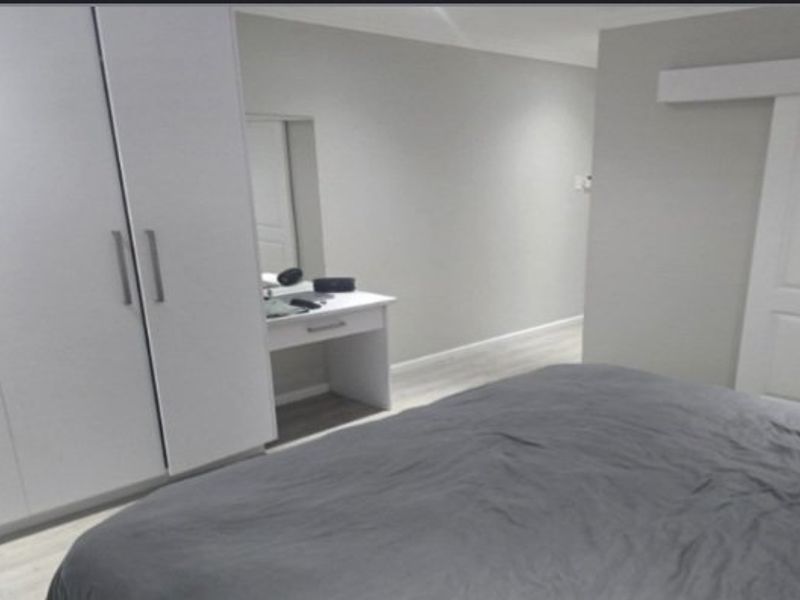 A modern bedroom featuring built-in cupboards, light laminate flooring, and a sliding door, presenting a clean and neutral aesthetic.