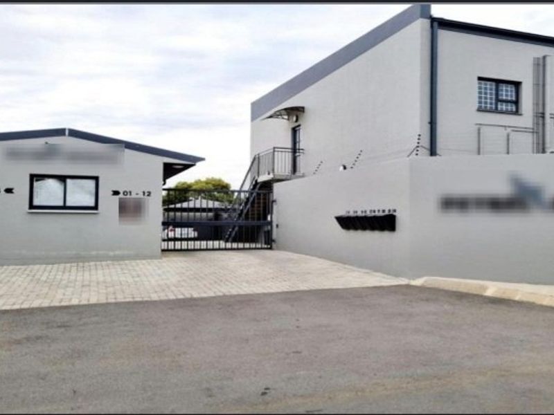 Front exterior view of the apartment complex featuring a paved driveway, secure gated entrance, external staircase, and wall-mounted post boxes.