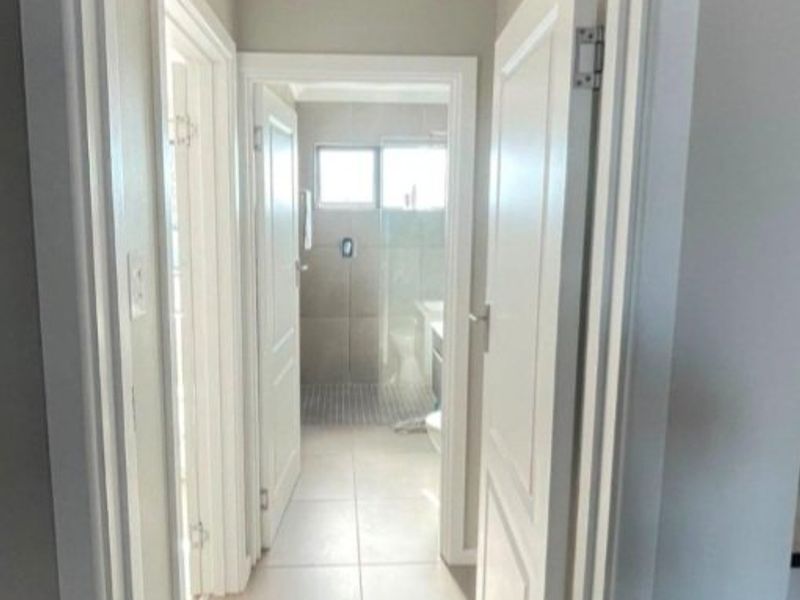 A clean, neutral hallway featuring tiled flooring and white internal doors, providing access to adjacent rooms including a bathroom.