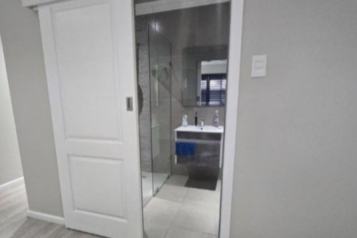 A modern bathroom featuring a sliding door entry, vanity cabinet with mirror, and a glass-enclosed shower with neutral tiled finishes.