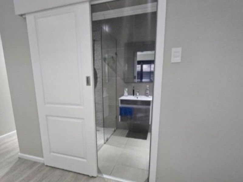 A modern bathroom featuring a sliding door entry, vanity cabinet with mirror, and a glass-enclosed shower with neutral tiled finishes.