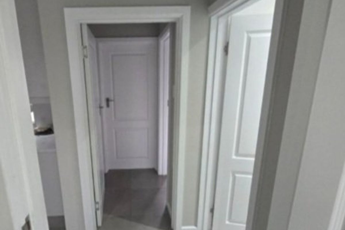 A clean and well-maintained hallway featuring neutral wall tones, tiled flooring, and white internal doors with matching architraves.
