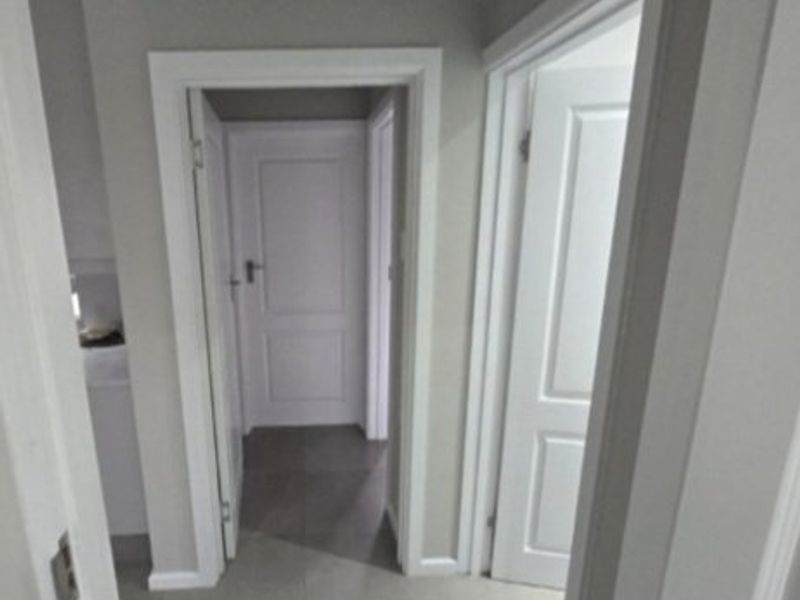 A clean and well-maintained hallway featuring neutral wall tones, tiled flooring, and white internal doors with matching architraves.