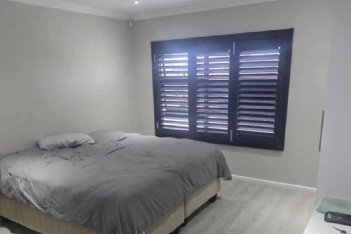 A well-maintained bedroom featuring modern laminate flooring, neutral wall tones, and dark plantation shutters that provide excellent light control and privacy.