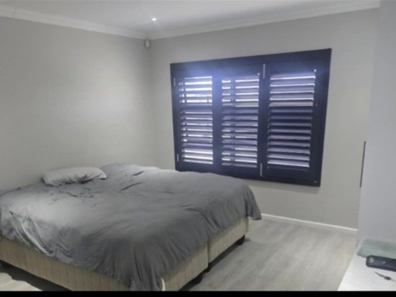 A well-maintained bedroom featuring modern laminate flooring, neutral wall tones, and dark plantation shutters that provide excellent light control and privacy.