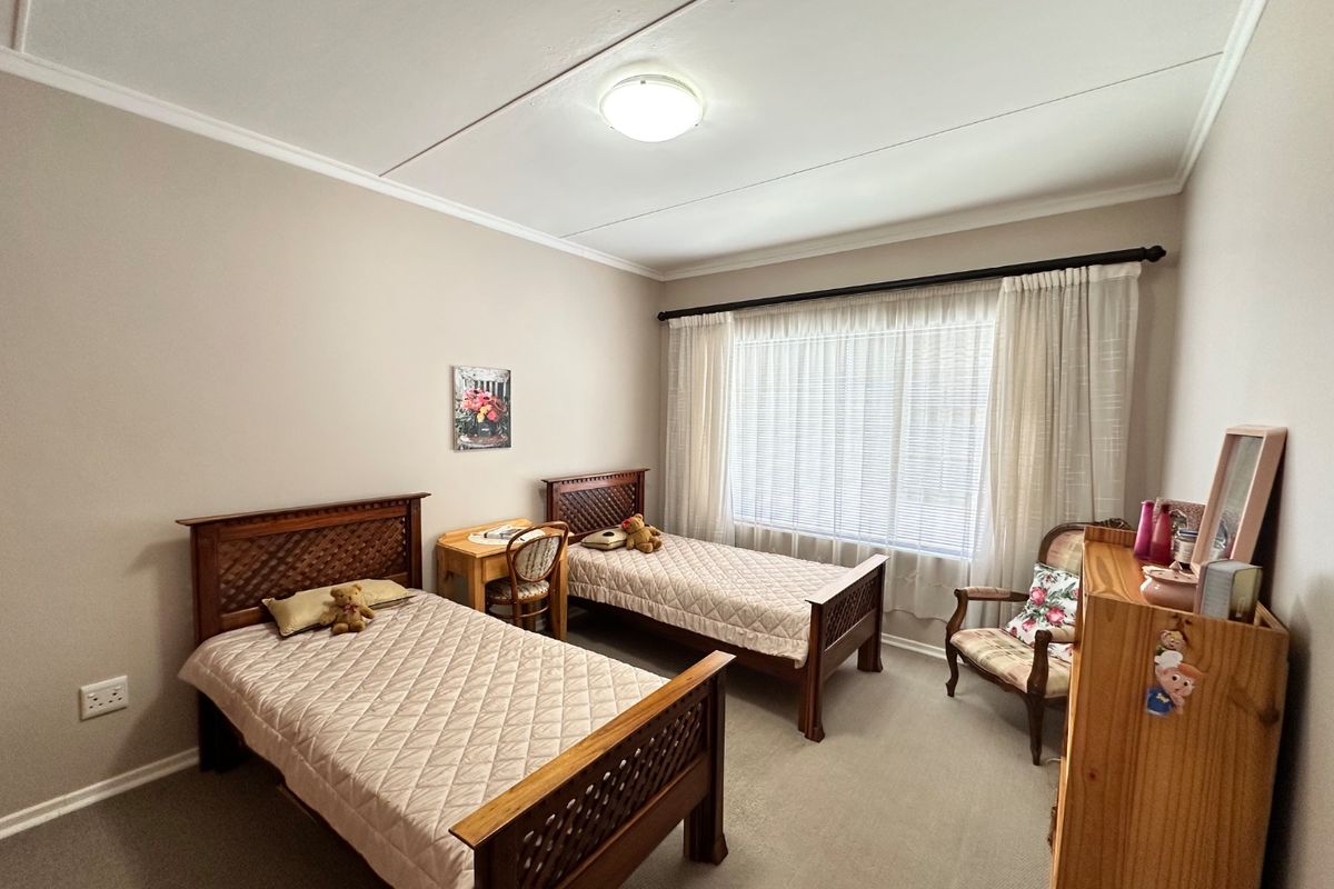 A well-maintained bedroom featuring neutral wall tones, carpeted flooring, and a large window with fitted curtain rods.