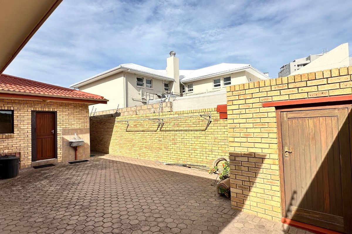 A paved rear courtyard area featuring face brick boundary walls, a wall-mounted washing line, and an external utility sink.