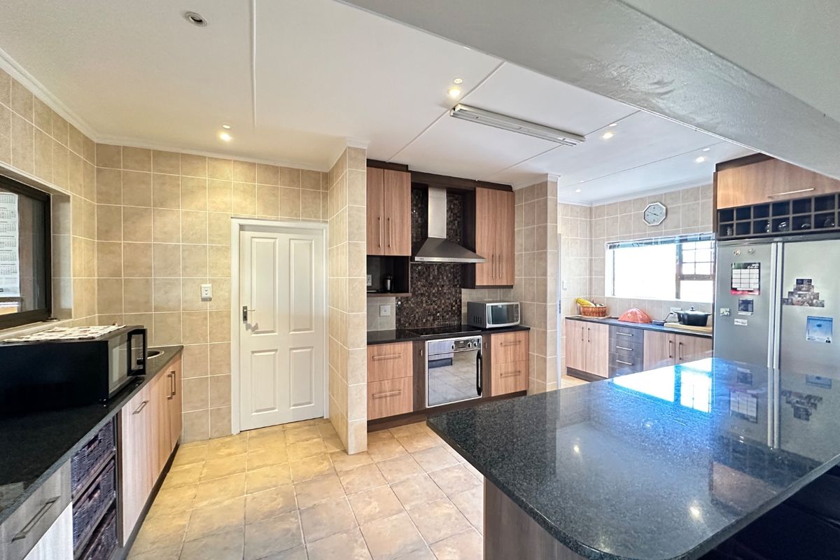 A spacious kitchen featuring granite countertops, built-in cabinetry, a stainless steel oven with extractor fan, and neutral tiled finishes throughout.