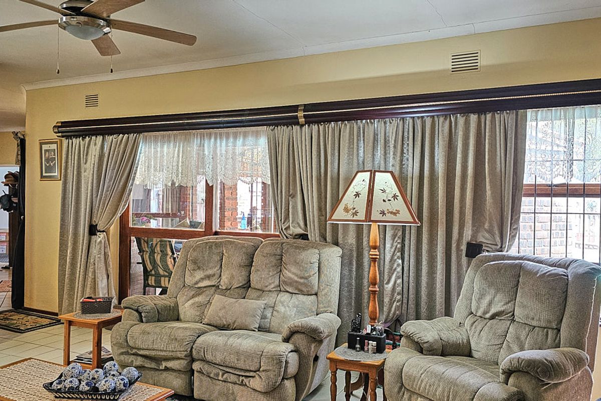 A comfortable living room featuring a ceiling fan, brick architectural detailing, and large windows with full-length curtains.