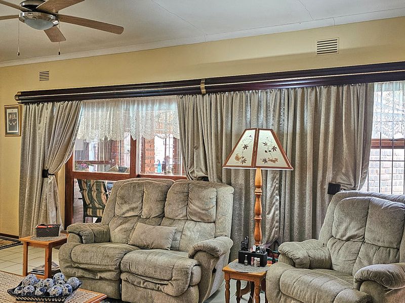 A comfortable living room featuring a ceiling fan, brick architectural detailing, and large windows with full-length curtains.