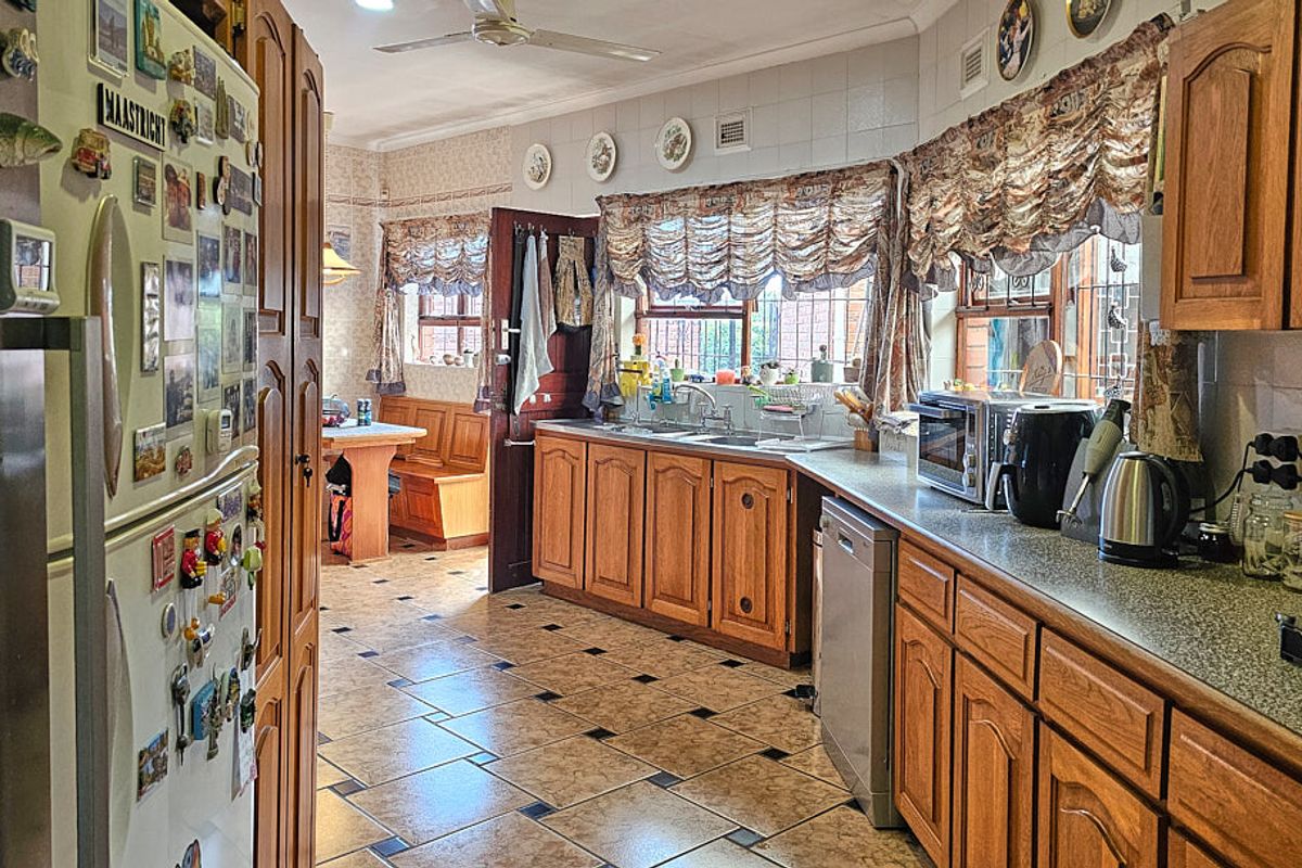 A traditional kitchen featuring wooden cabinetry, laminate countertops, a double basin sink, and tiled flooring, with an adjacent dining nook area.