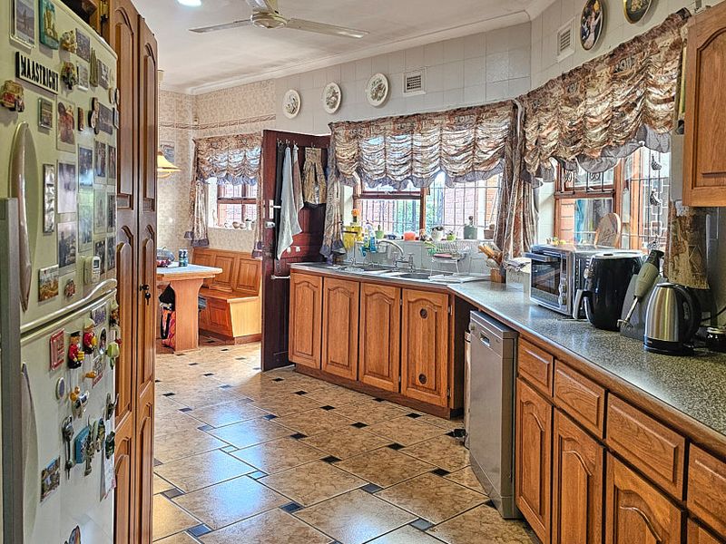 A traditional kitchen featuring wooden cabinetry, laminate countertops, a double basin sink, and tiled flooring, with an adjacent dining nook area.