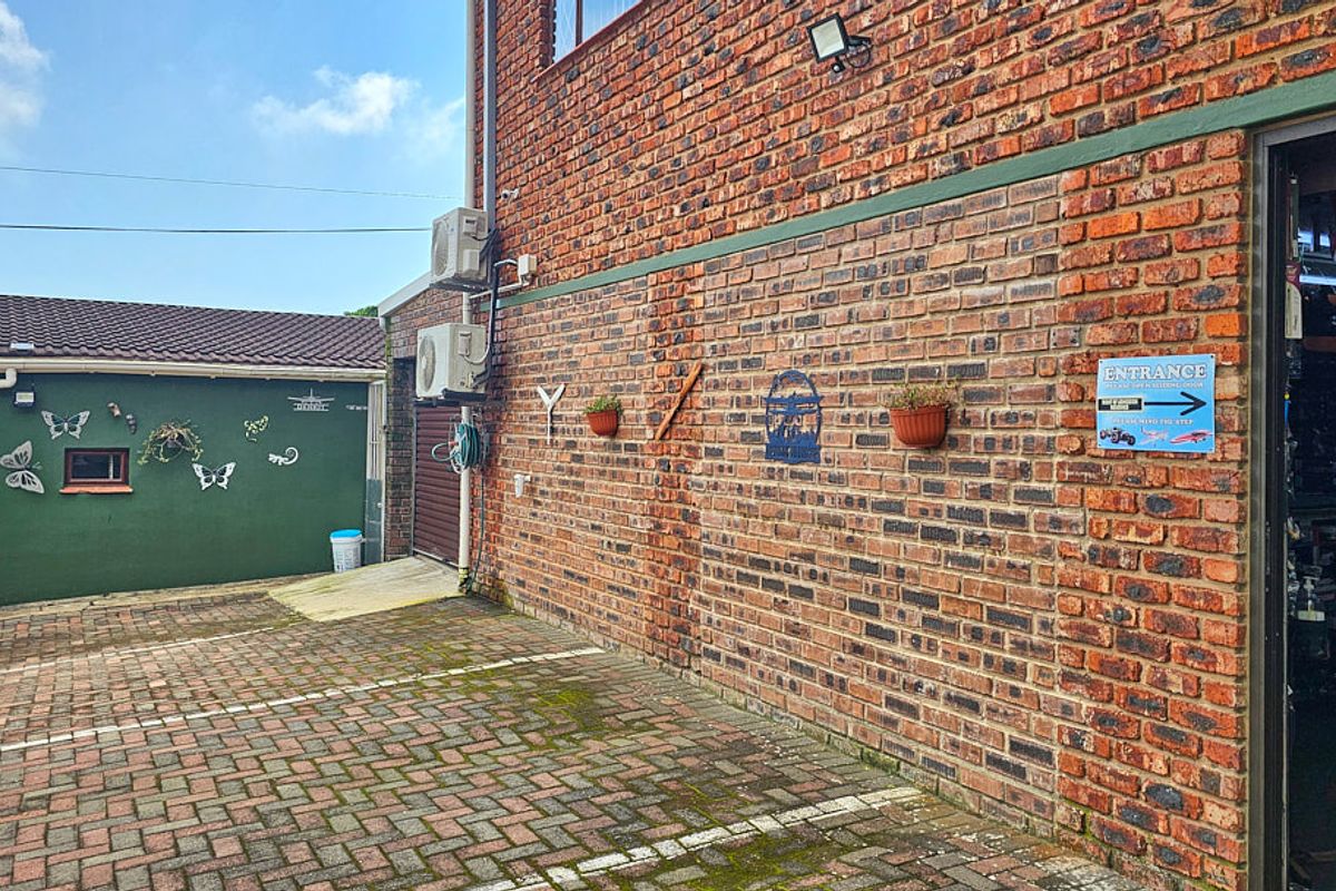 A paved exterior area featuring a brick facade, mounted air conditioning units, and security lighting, providing access to the building entrance.