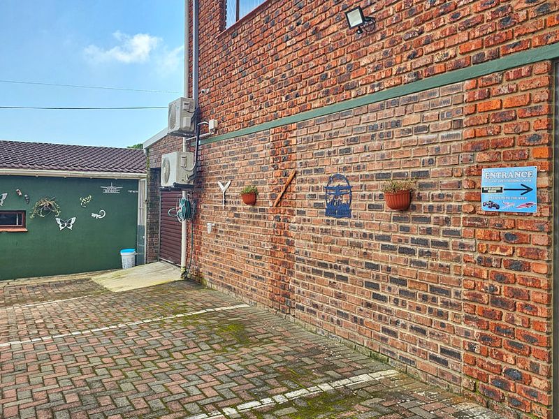 A paved exterior area featuring a brick facade, mounted air conditioning units, and security lighting, providing access to the building entrance.
