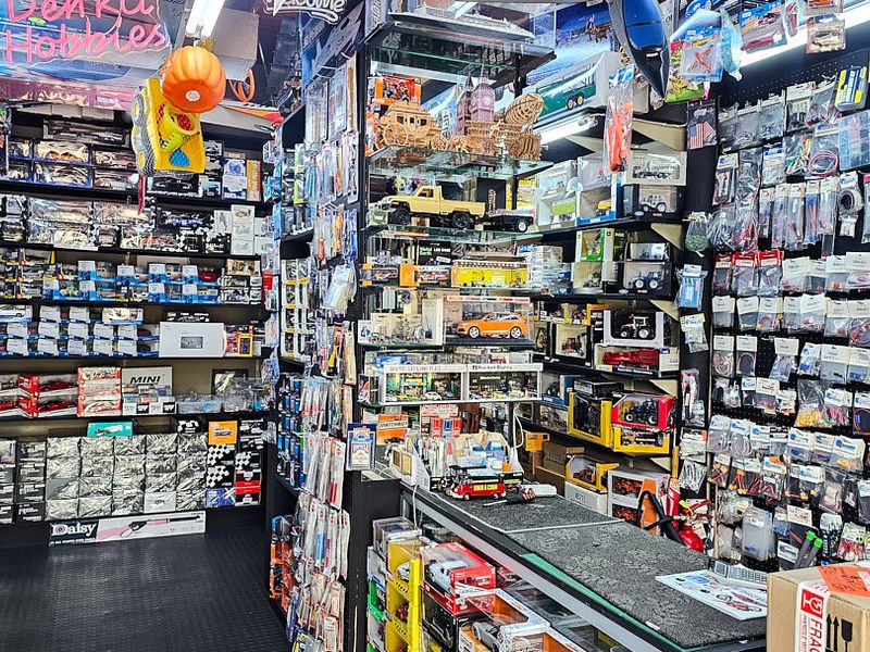 A commercial retail space featuring extensive built-in shelving units, overhead fluorescent lighting, and durable rubber flooring, currently utilized for hobby product display.