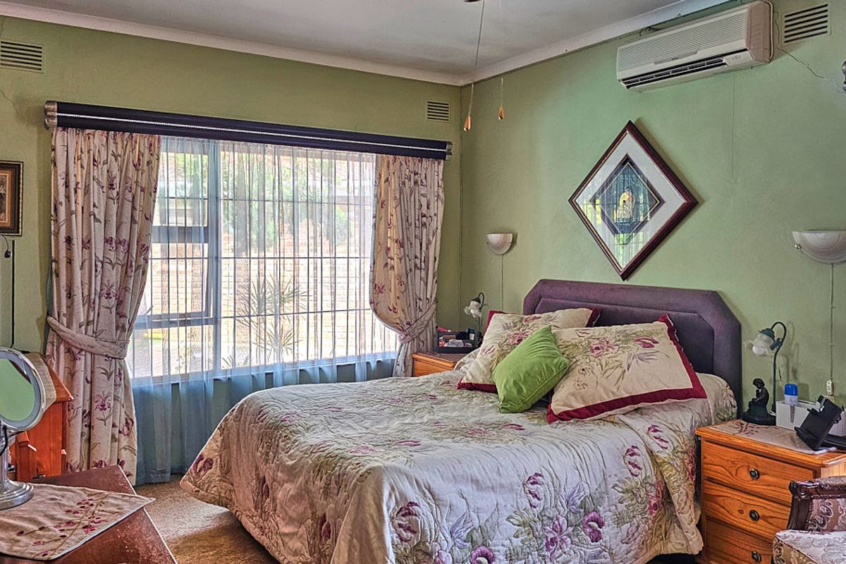 A bedroom featuring a split-system air conditioner, wall-mounted lighting, and a large window with security bars, finished with carpeted flooring.