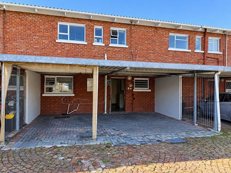 Front exterior view of a brick townhouse featuring a paved driveway, covered carport, and secure metal gate access.