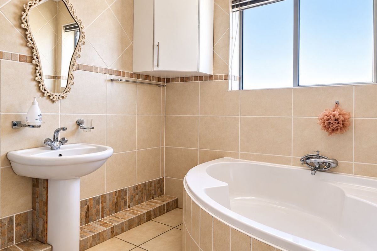A clean bathroom featuring a pedestal basin, a built-in bathtub with tiled surround, and neutral wall tiling.