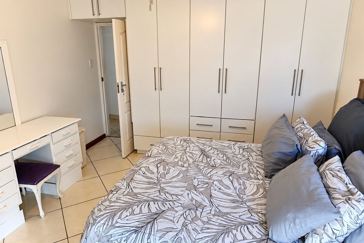 A well-maintained bedroom featuring extensive built-in cupboards with overhead storage, tiled flooring, and a ceiling fan.