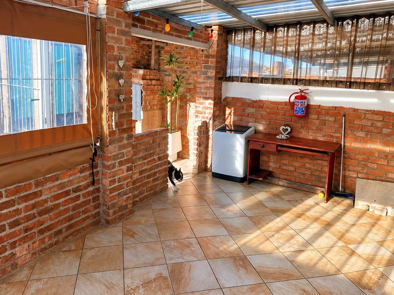 Covered patio area featuring exposed brick walls, tiled flooring, and roll-down weather blinds, providing a versatile outdoor living space.