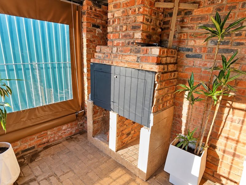 Covered patio area featuring a built-in brick braai and durable paved flooring, enclosed with a retractable weather blind for year-round outdoor entertainment.
