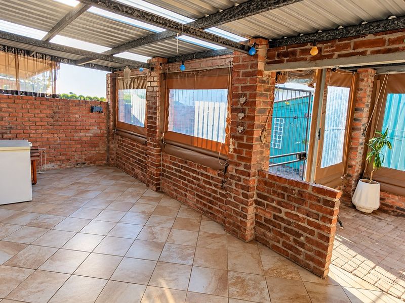 A covered outdoor patio area featuring exposed brick walls, tiled flooring, and roll-up weather blinds, providing a versatile space for outdoor living.