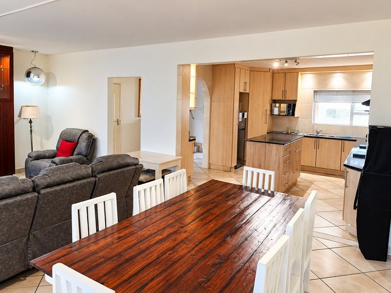 Open-plan living and dining area featuring a well-appointed kitchen with light wood cabinetry, stone countertops, and a central island, finished with neutral tiled flooring.