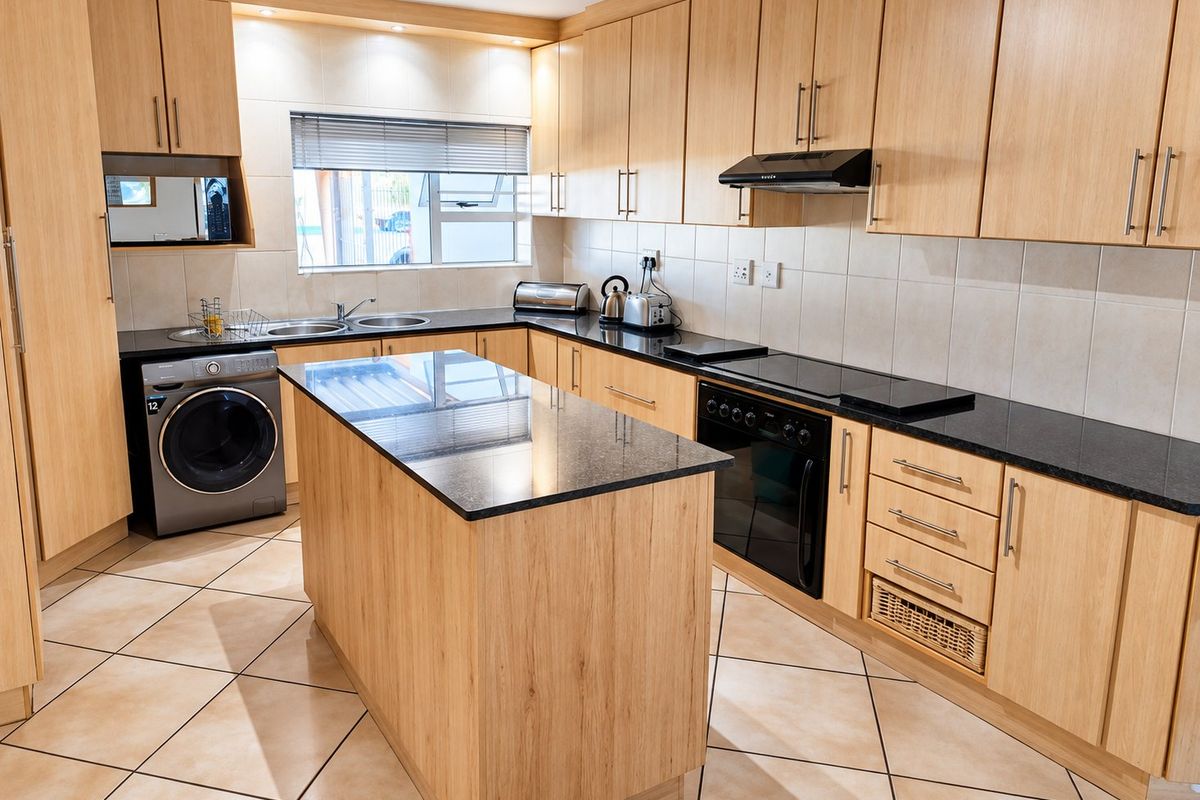 A well-maintained kitchen featuring light wood cabinetry, granite countertops, a central island, and integrated appliances with tiled flooring and backsplash.