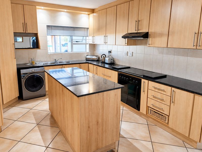 A well-maintained kitchen featuring light wood cabinetry, granite countertops, a central island, and integrated appliances with tiled flooring and backsplash.