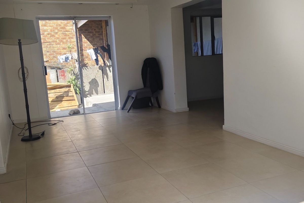 An empty living room featuring neutral tiled flooring and a sliding glass door providing access to an outdoor area.