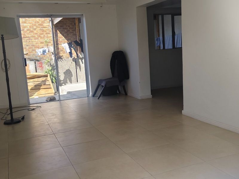 An empty living room featuring neutral tiled flooring and a sliding glass door providing access to an outdoor area.