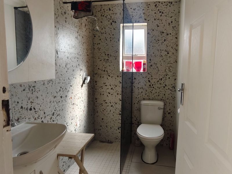 A functional bathroom featuring terrazzo-style wall tiling, a walk-in shower with a glass screen, a pedestal basin, and a standard toilet.