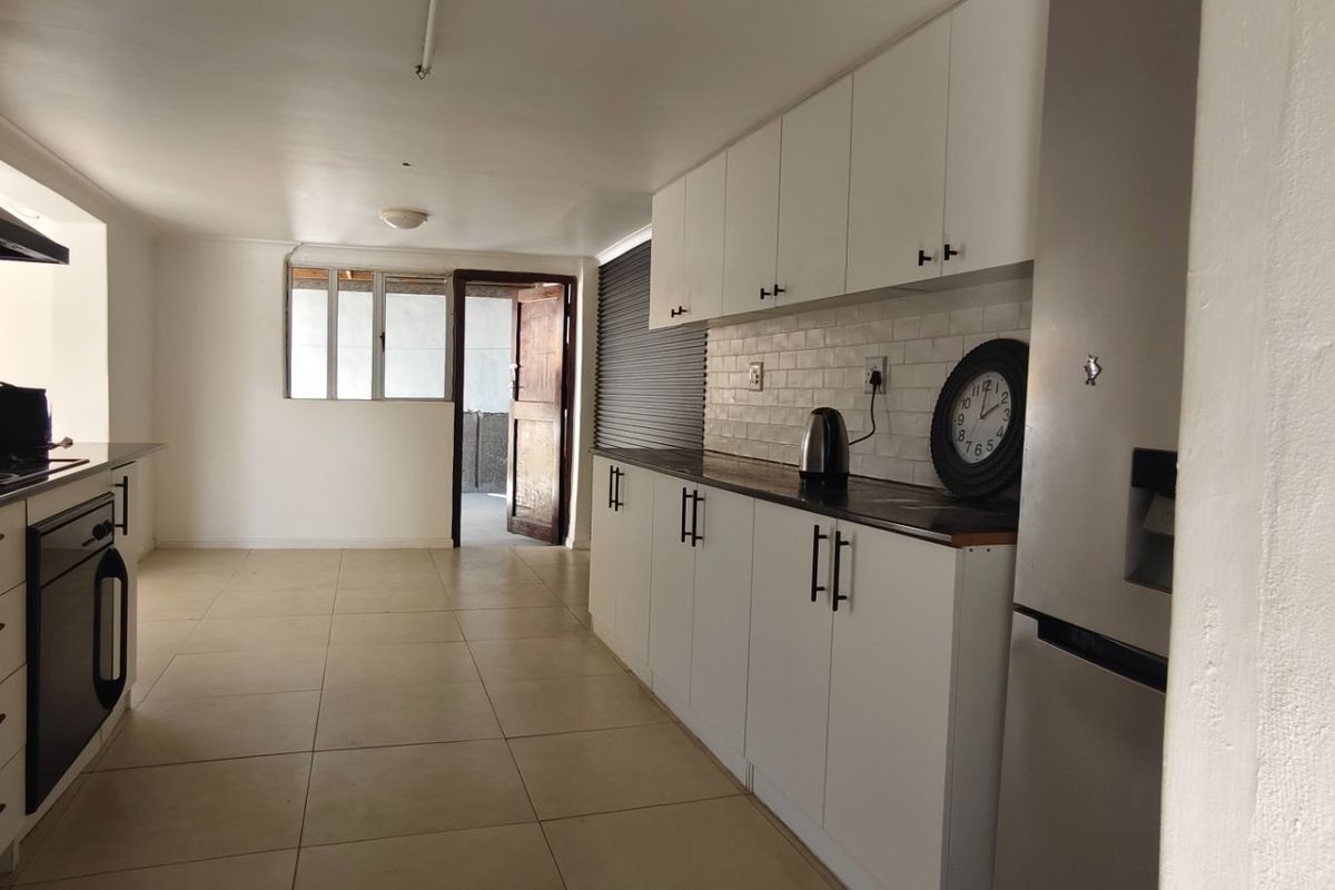 A functional kitchen featuring white cabinetry, dark countertops, a built-in oven, extractor fan, and tiled flooring with direct access to an outdoor area.