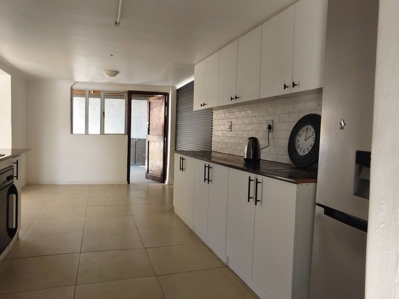 A functional kitchen featuring white cabinetry, dark countertops, a built-in oven, extractor fan, and tiled flooring with direct access to an outdoor area.