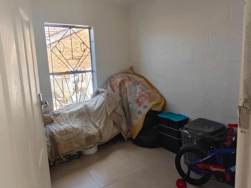 A small bedroom featuring tiled flooring and a window fitted with security bars, currently used for storage.