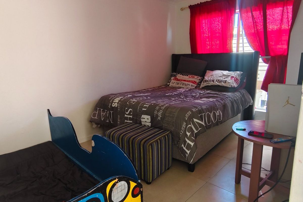 A standard bedroom featuring tiled flooring and a window with red curtains, providing a functional space for rest.
