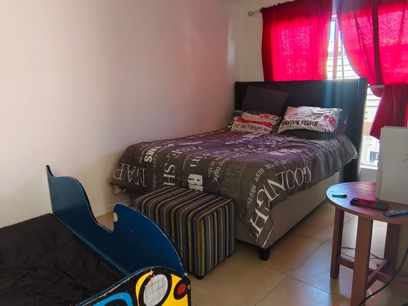 A standard bedroom featuring tiled flooring and a window with red curtains, providing a functional space for rest.