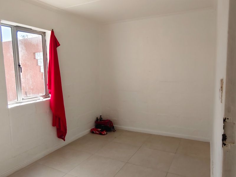 A simple, empty bedroom featuring tiled flooring and an aluminium window frame, offering a blank canvas for potential interior design updates.