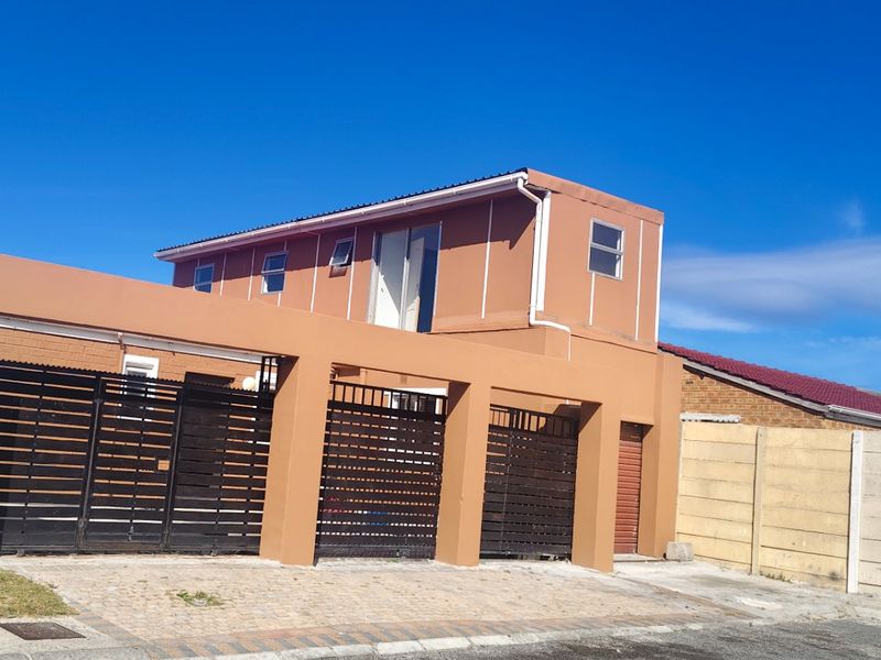 Front exterior view of a two-story house featuring a paved driveway, integrated carport with sliding gates, and a precast concrete boundary wall.