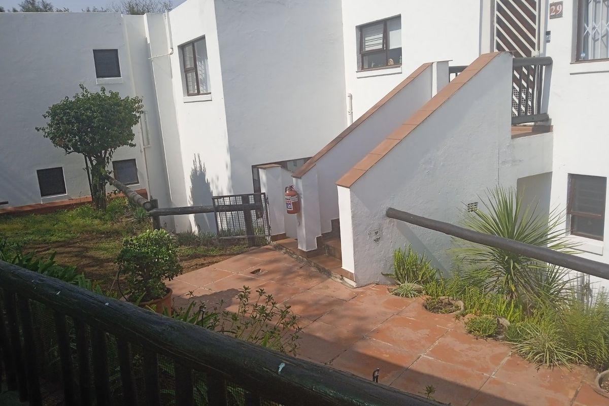 Exterior view of an apartment complex featuring a terracotta tiled patio area, concrete staircase, and white rendered walls with security fixtures.