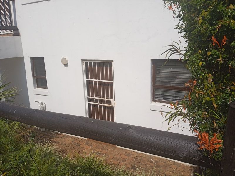 Rear exterior view of the apartment featuring a security gate, window blinds, and a paved walkway area.