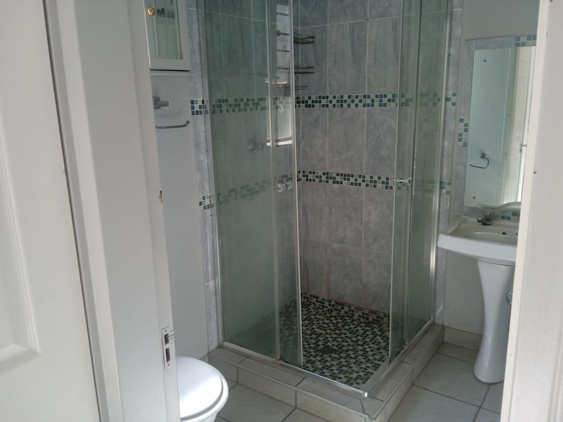 A functional bathroom featuring a glass-enclosed shower with mosaic tile accents, a pedestal basin, and a wall-mounted mirror.