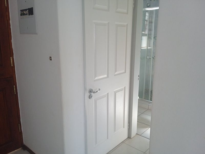 A functional hallway area featuring tiled flooring, a white panel door, and a wall-mounted electrical distribution board, providing access to an adjacent bathroom.