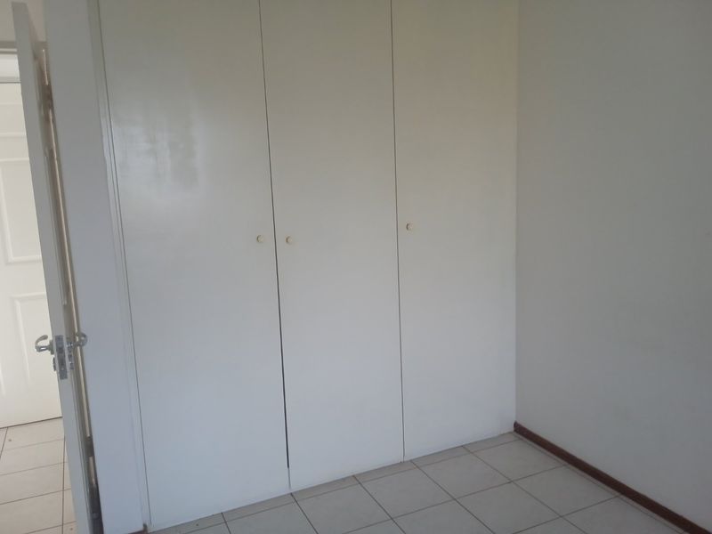A simple bedroom featuring neutral tiled flooring and white built-in cupboards, offering a clean and functional space ready for personalization.